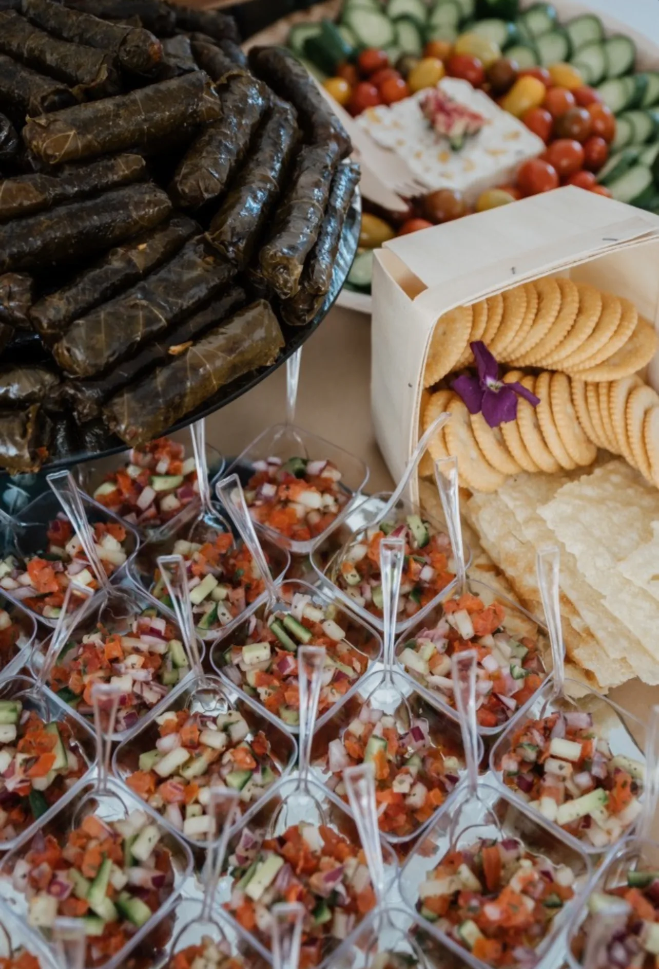 Savory appetizer cups, dolma, cheese, tomatoes, and crackers on an event table